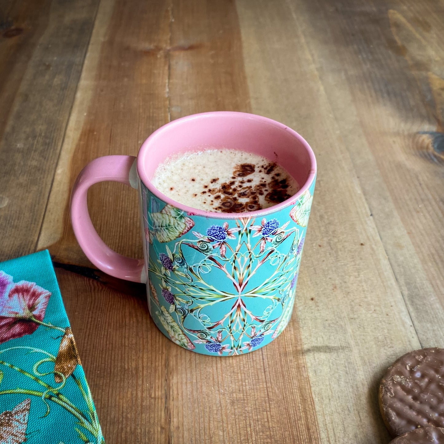 Decorative turqouise and pink mug with floral pattern on a wooden surface