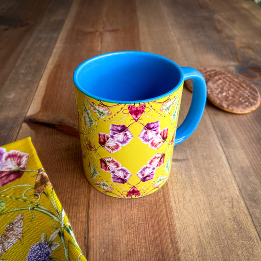 Yellow mug with floral pattern and blue handle on a wooden surface