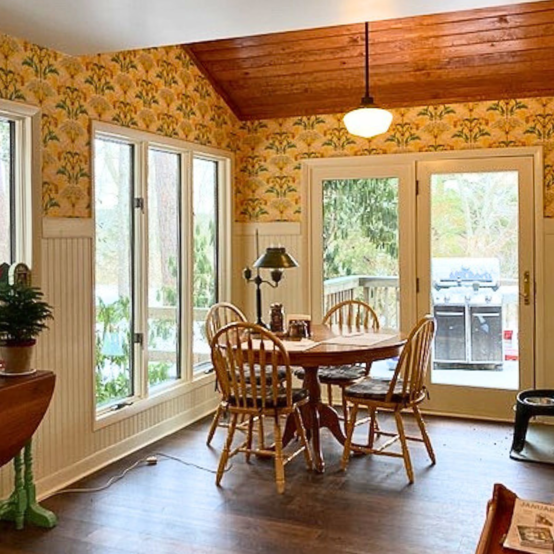 Customer Kitchen in Viriginia, USA. It has yellow Catkin Hemlock wallpaper on the upper parts of the walls, and cream coloured woodwork. The floor is and ceiling are dark wood and there is a  circular pine arts and crafts style dining table in the middle of the room with four chairs