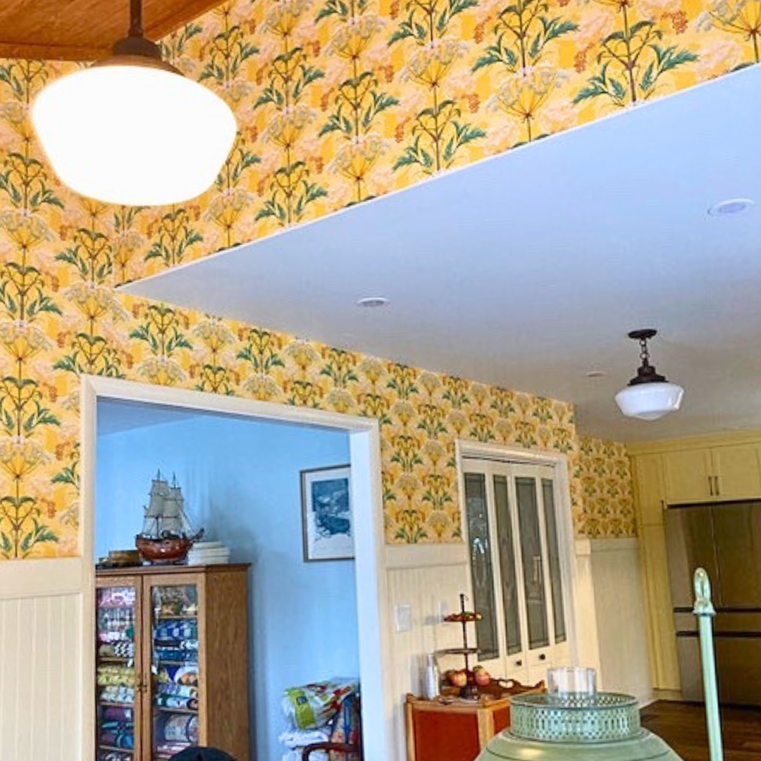 Customer Kitchen in Viriginia, USA. It has yellow Catkin Hemlock wallpaper on the upper parts of the walls, and cream coloured woodwork. There is a vaulted ceiling which is panelled with dark wood and arts and crafts style lamps hanging from the ceiling.