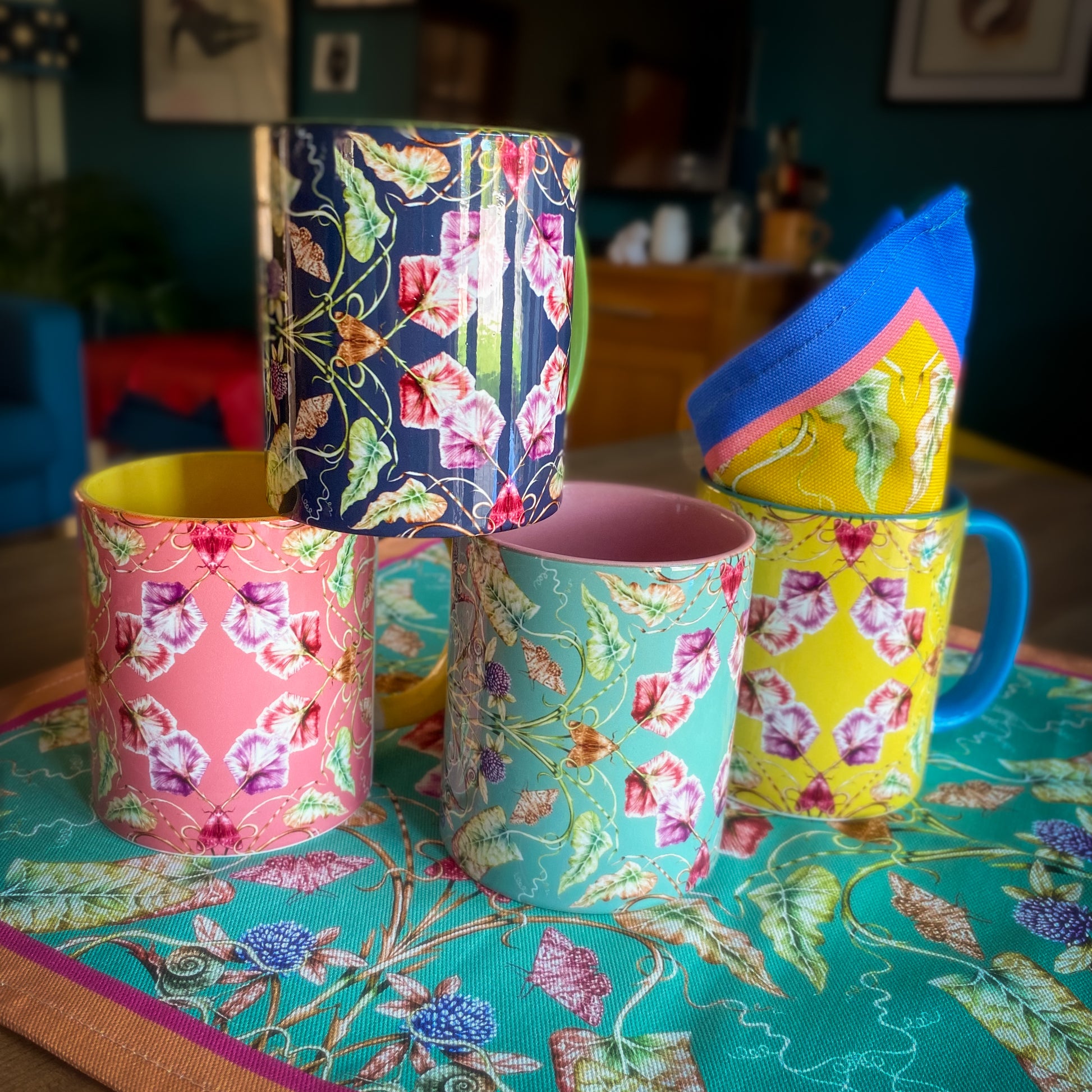 Colorful floral-patterned mugs on a table with a patterned tablecloth. April Mawhinney Illustration
