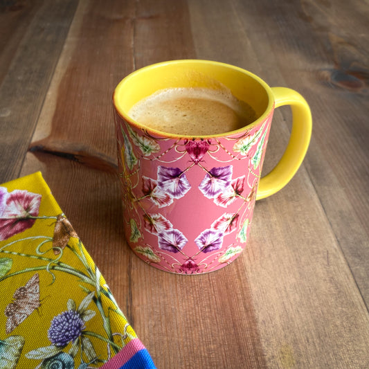 Pink mug with floral pattern and yellow handle filled with coffee on a wooden surface