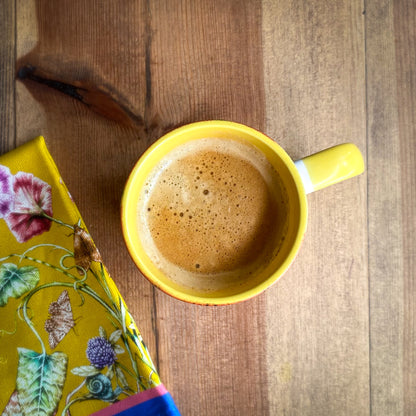Yellow mug with a hot beverage on a wooden surface next to a floral napkin
