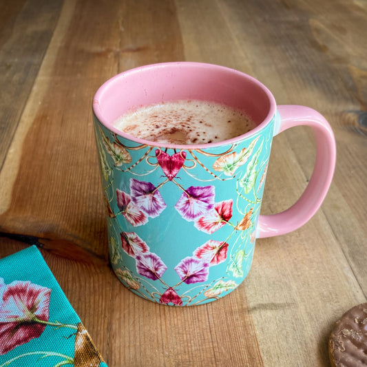 Floral-patterned mug with pink handle on a wooden surface