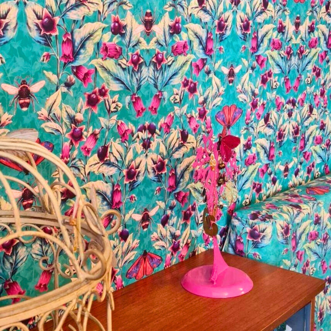 Walls of guest bedroom papered in Deadly Nightshade Arsenic Wallpaper. The wallpaper has a background colour of turquoise, and overlaid with bees, red and purple cinnabar moths.There are entwining purple berries and magenta flowers.